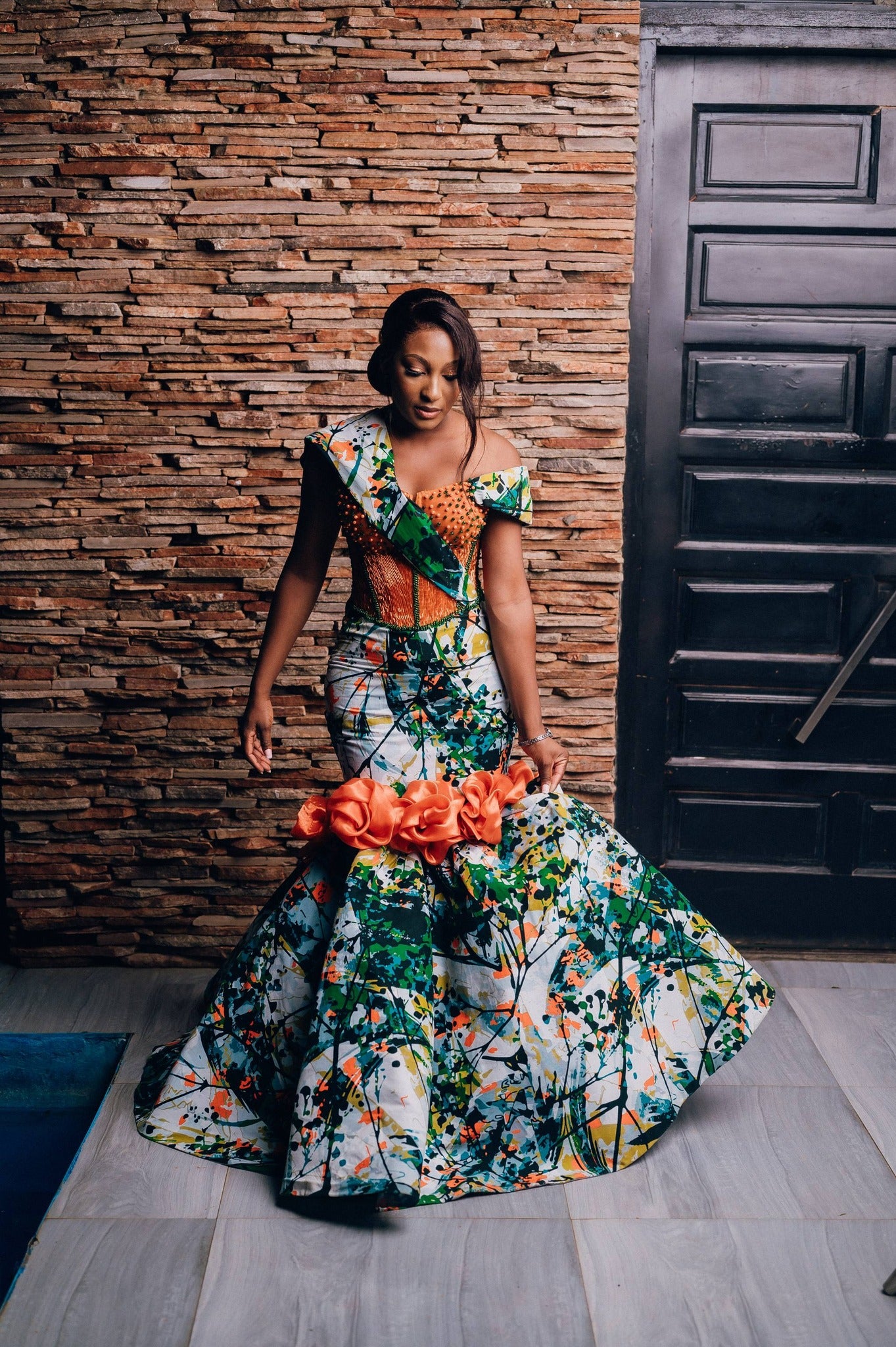 Woman in a colorful floral dress standing against a textured wall.